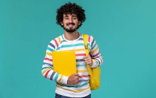 front-view-male-student-wearing-yellow-backpack-holding-files-blue-wall